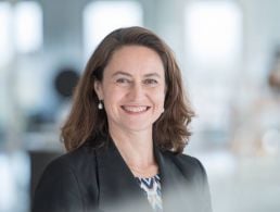 A woman with brown hair and glasses smiles at the camera in front of a grey background. She is Katherine Conway, global head of inclusion and cultural initiatives at Aon.