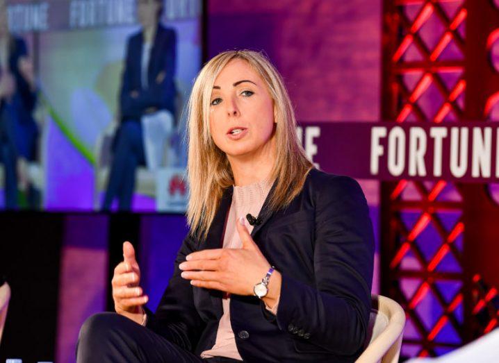 A woman in a black coat sitting on a stage and speaking. She is Irish Data Protection Commissioner Helen Dixon.