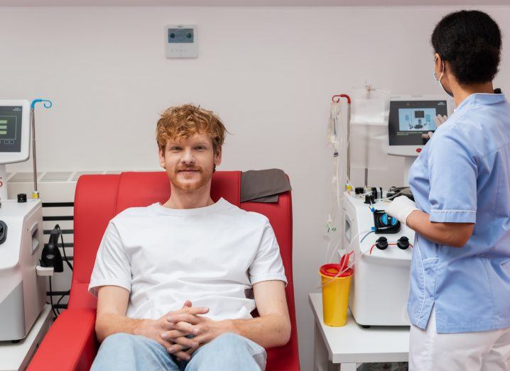 Patient seated in a chair while a healthcare professional uses tech equipment on the side.