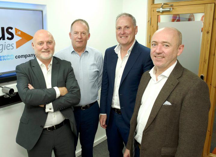 Four men in business attire stand in a group in an indoor space.