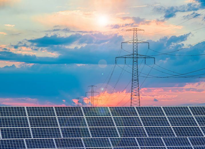 Solar panels with electricity lines visible amid the sunset in the background.