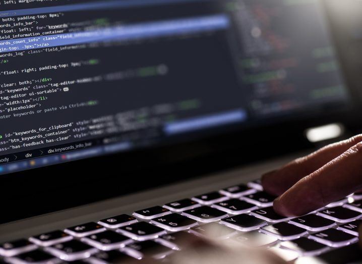 Close-up of a person's hands typing on a laptop keyboard with code visible on the screen.