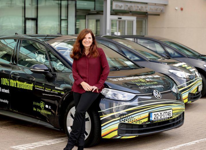 A woman leans against a car that is used by Siro.