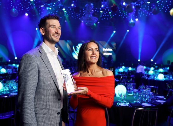 A man and a woman receive an award on stage at a ceremony.