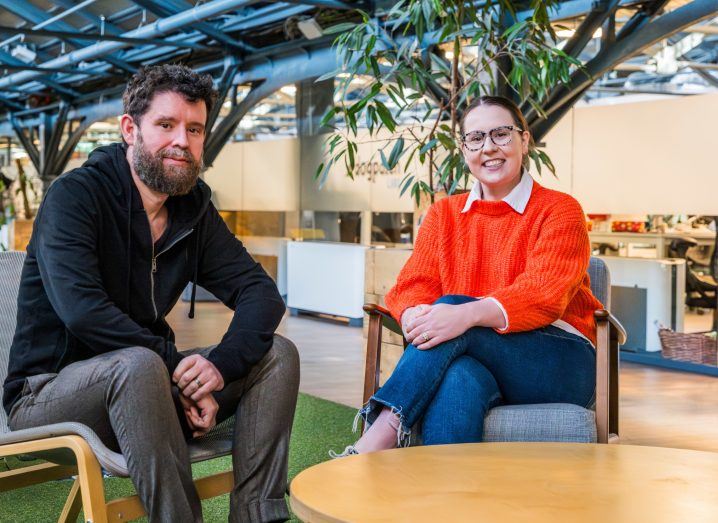 A man and a woman sit next to each other in an indoor space.