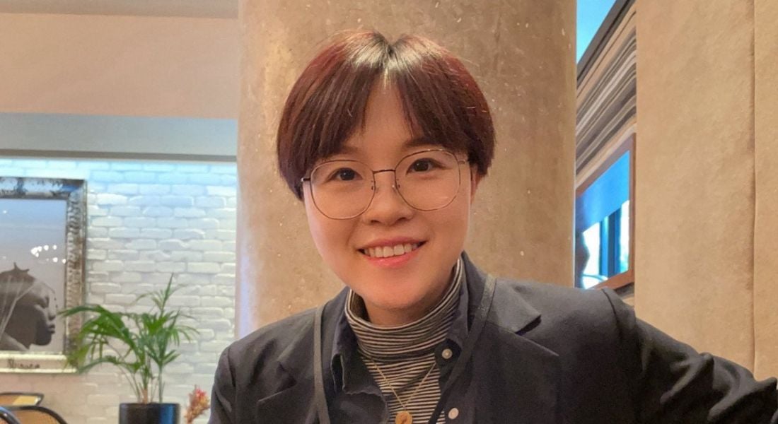 A woman with short hair and glasses smiles at the camera in an office setting. She is Addison Ying, a principal data analyst at Fidelity Investments.