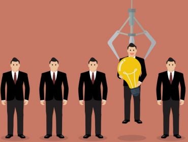 Cartoon showing a row of jobseekers in suits and one is being picked up by a robotic hand. He is holding a lightbulb.