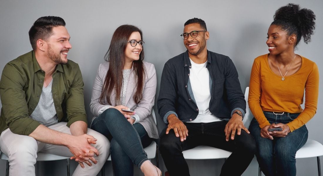 A group of four happy workers sitting in a row on chairs chatting together.