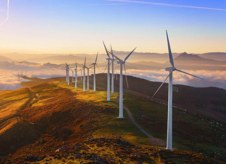 A row of wind turbines on a hill with clouds in the distance.