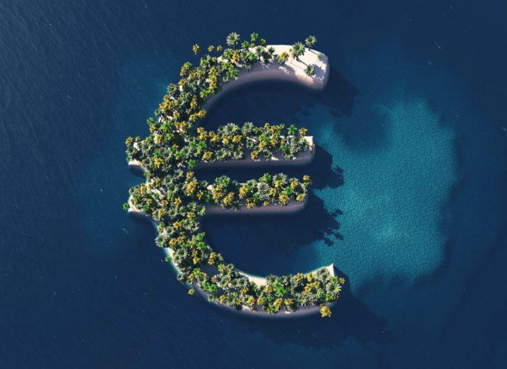 Aerial image of an island in the shape of a euro sign, with green trees growing on it and blue water surrounding it.