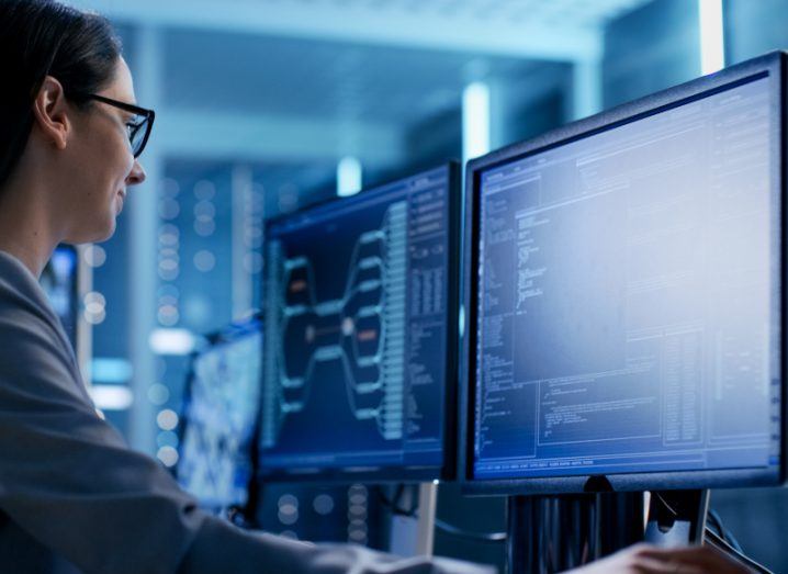 A woman wearing glasses sits in front of a computer scanning code on the screen. There are more computers in the background.