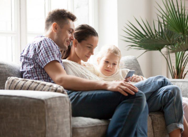 A man and a woman with a young teen sitting together on a couch using a phone.