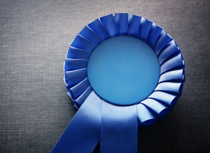 A blue award ribbon laying on a grey surface.