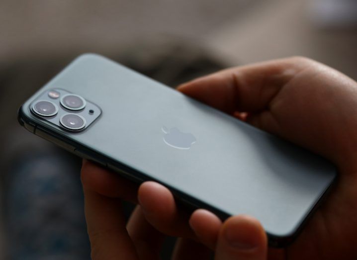 An iPhone in a person's hand, with the Apple logo visible on the back of the device.