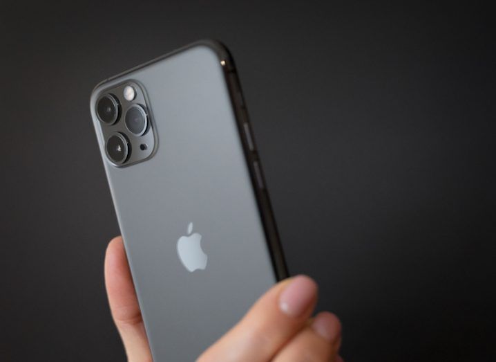 An apple iPhone in a person's hand, with a dark background.