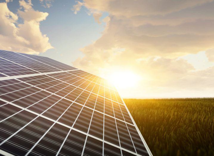 A solar energy panel on a field, with the sun, sky and clouds visible in the background.