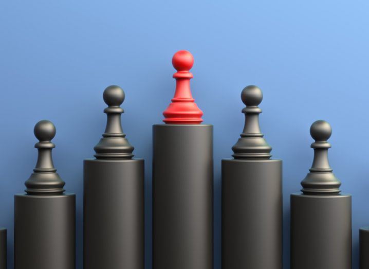 Leadership concept with chess pieces on black pillars. There is one red chess piece on the centre, highest black pillar signifying the leader. The background is blue.