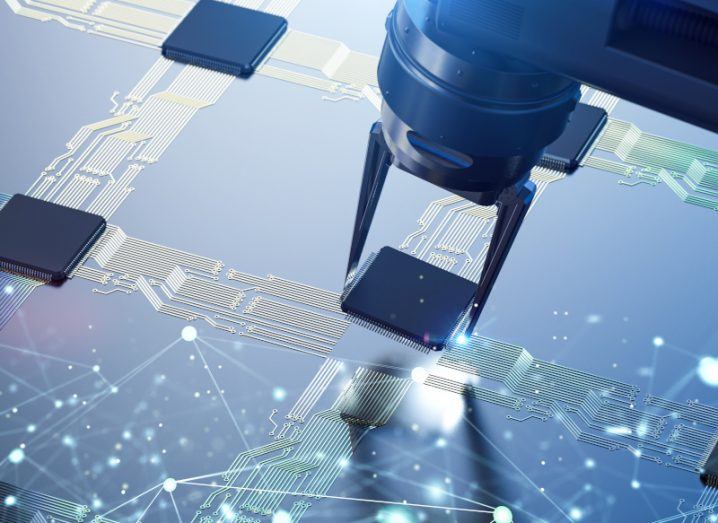 A robotic arm pincering a semiconductor chip and placing it on a board.