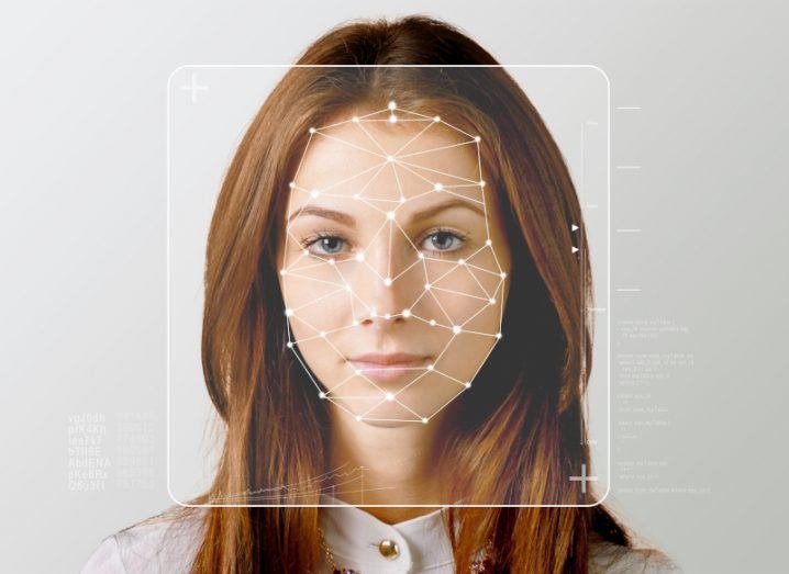 A woman looking forward with white dots around parts of her face, standing in front of a grey background. Used as a concept for facial recognition technology.