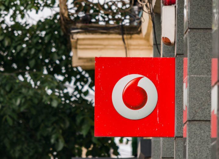 The Vodafone logo on a red sign hanging from the side of a building.