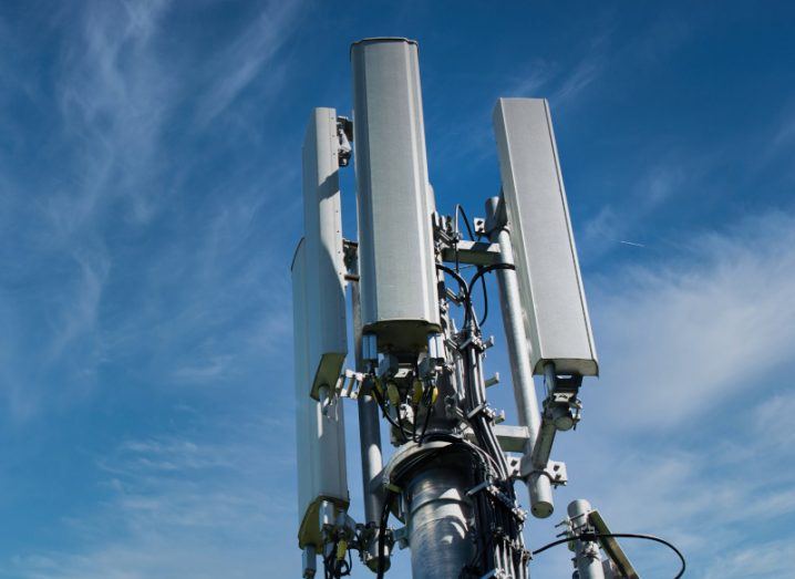 A mobile phone network tower with a blue sky and light grey clouds in the background.