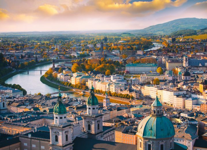 Skyline of an Austrian town during sunset. A river flows through the town and mountains can be seen in the background.