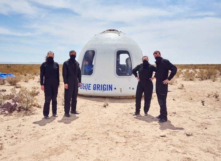 Four people stand in a desert beside a pod that says 'Blue Origin'.