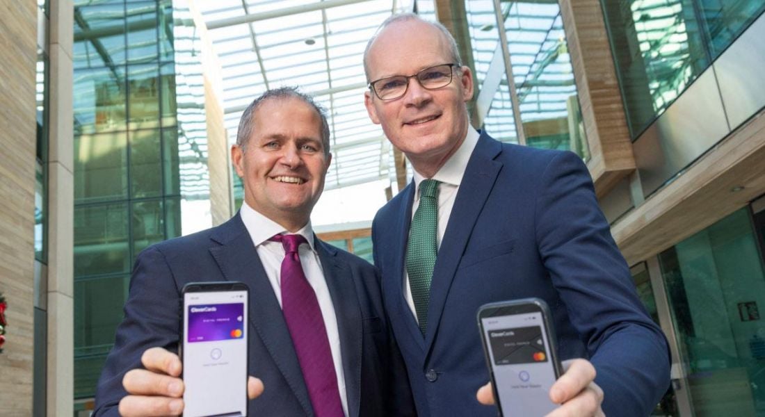 Two men stand side by side looking down at the camera while holding phones that show the CleverCards app in action.