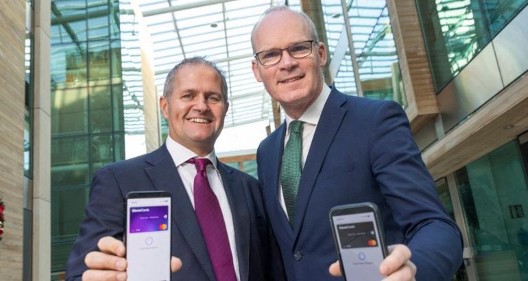 Two men stand side by side looking down at the camera while holding phones that show the CleverCards app in action.