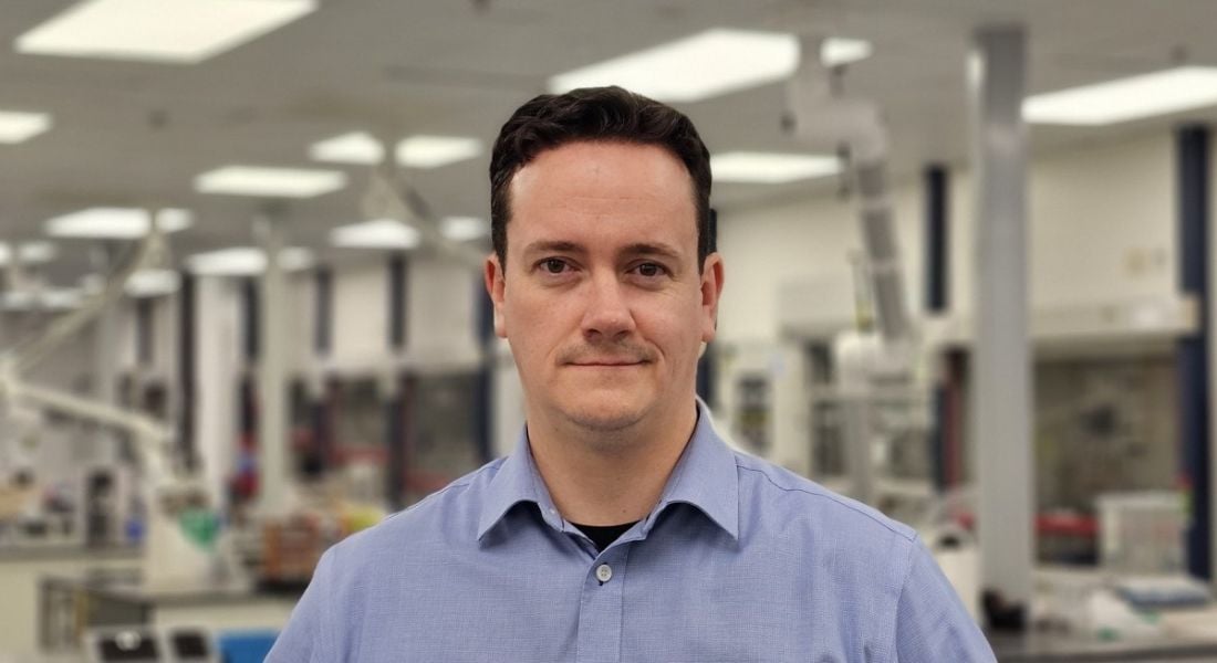 A man wearing a blue shirt smiles at the camera in a lab setting. He is Cormac Duffy, a scientific principal at Henkel.