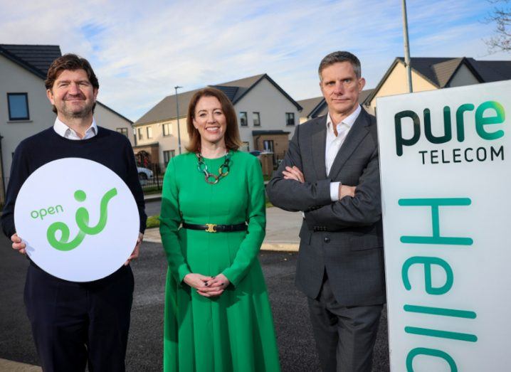 Two men and one woman standing together with houses in the background. One of the men is holding a circular sign that says Open Eir on it, while the other man is next to a sign that has the Pure Telecom logo on it.