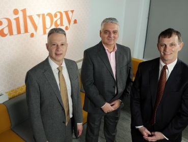 Three people standing in front of a wall with DailyPay logo on it in orange print.