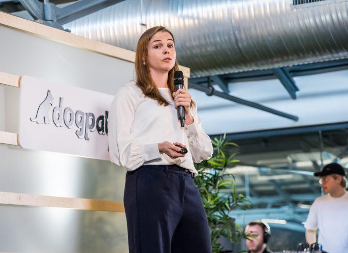 A woman stands on a stage with a mic in her hand. Dogpatch Labs logo in the background.