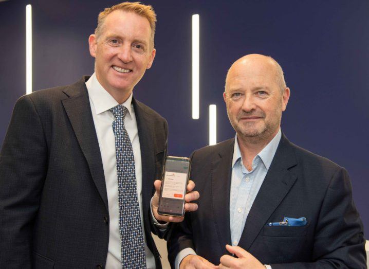 Two men in suits standing together, with one holding a phone in his hand. They are part of Permanent TSB and Expleo.