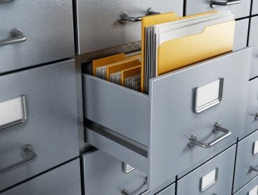 A folder containing files sticks out of an opened drawer of a grey filing cabinet.