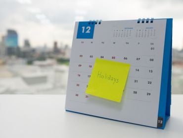 A calendar with a sticky note sits next to a window where a city skyline can be seen. The word 'Holiday' is written on the sticky note.