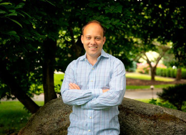 A man wearing a light coloured shirt smiles with his arms folded while standing in front of a tree. He is Ian White, CEO, CTO and founder of ChartHop.