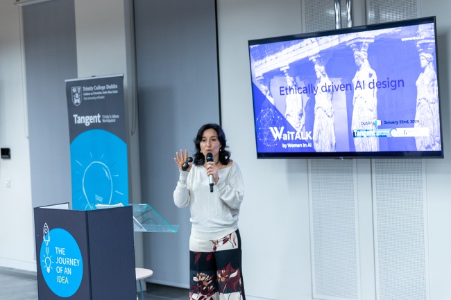 Alessandra Sala holds a microphone and speaks in front of a screen for a women in AI event at Trinity Business School