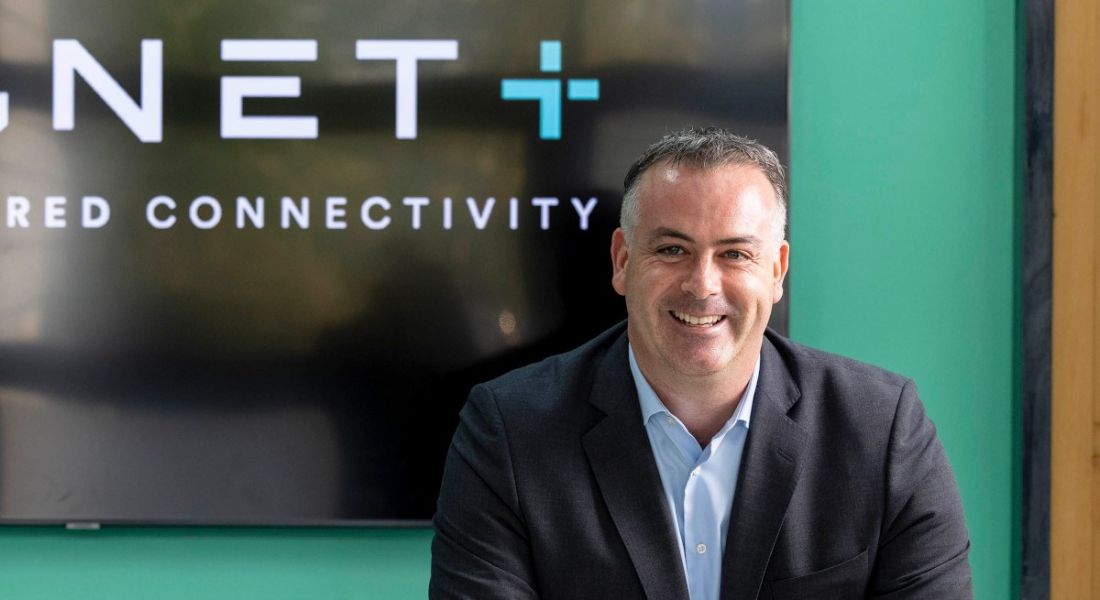 A man in a suit smiling at the camera. Behind him is a wall that shows the second half of the Magnet Plus logo.