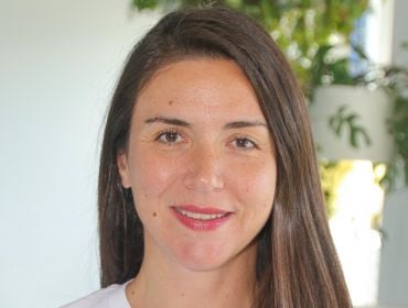 A woman with long brown hair smiles at the camera in front of a white wall and a large plant. She is Maria Duni, the country manager for the Nordics at Personio.