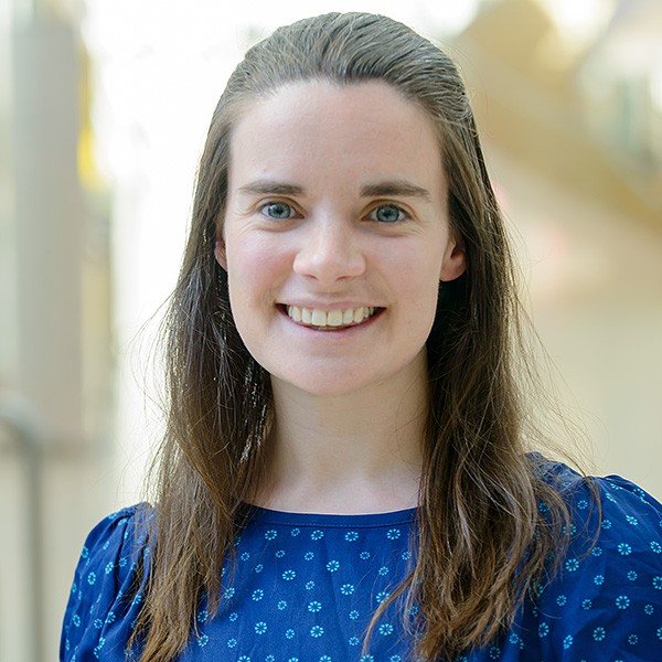 A headshot of Dr Muireann Lynch who smiles at the camera. She has long brown hair and wears a blue blouse and the background is blurred.