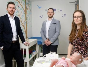 The three NeuroBell co-founders in a nursery with a baby doll in a child's cot.