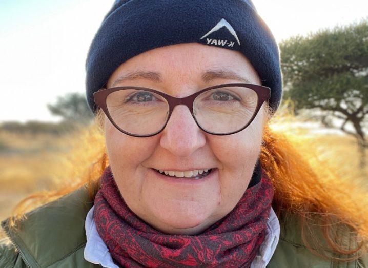 A woman wearing a hat and a brown coat, with trees in the background. She is Dr Niamh Shaw.