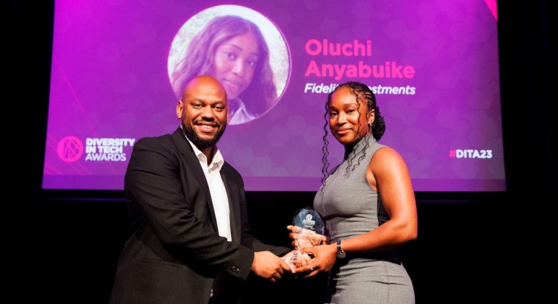 A man wearing a suit presents an award to a women in a grey dress in front of a purple screen displaying the details of the award and awardee. The woman is Oluchi Anyabuike, a senior software engineer.