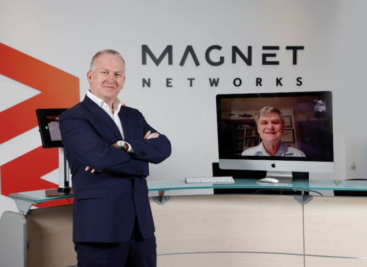 Speed Fibre Group CEO Peter McCarthy stands next to a screen hosting a video call to Ken Peterson. He is in a Magnet Networks office.