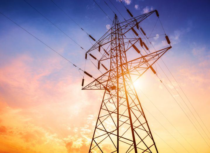 A photo of power lines and tower taken from below at sunset.