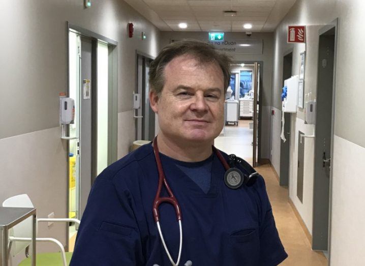 A man in a blue medical shirt standing in a hallway. He is Professor Austin Stack of the University of Limerick.