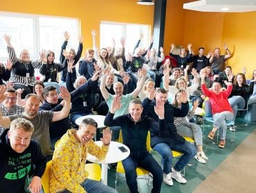 A crowd of people in the new office opened by Scurri, they are raising their arms in the air in celebration.