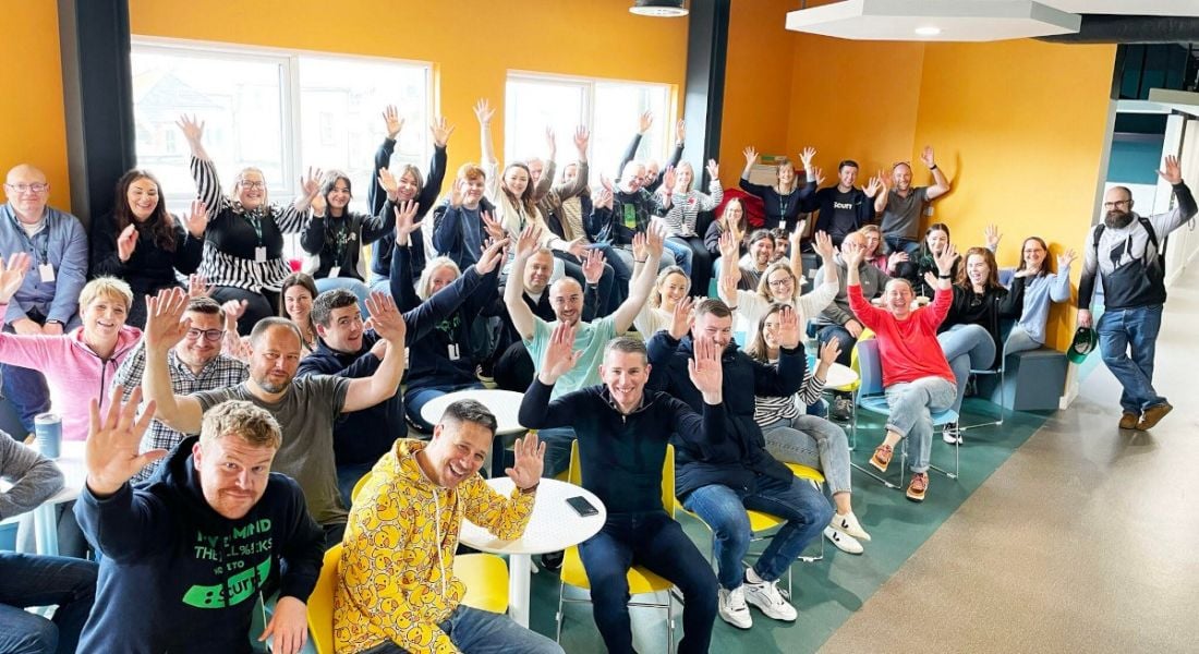 A crowd of people in the new office opened by Scurri, they are raising their arms in the air in celebration.