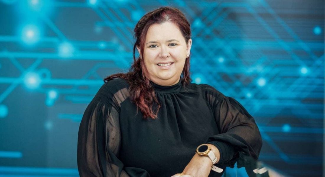 A woman smiles at the camera while resting her left elbow on a counter. There is a digital graphic behind her. She is Tricia Cahill, a cloud software engineer at Intel.